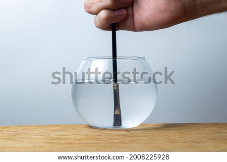 A paintbrush is dipped in a jar of water on a white background. Hand holding bone for drawing