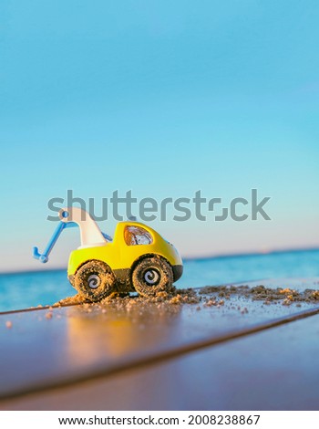 A children's construction machine is all covered in sand against the background of a pond and a blue sky. Construction concept.