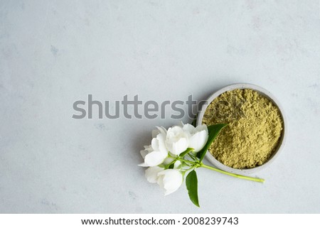 henna powder for dyeing hair and eyebrows and drawing mehendi on hands on a gray cement pedestal with dried flowers or a white flower.