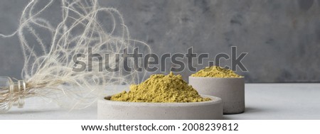 Banner. henna powder for dyeing hair and eyebrows and drawing mehendi on hands on a gray cement pedestal with dried flowers or a white flower.