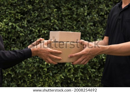 Man's hand taking blank recycled paper cardboard box shopping from woman with outdoor green leaves nature garden background. Delivery boxes mockup for branding design concept Royalty-Free Stock Photo #2008254692