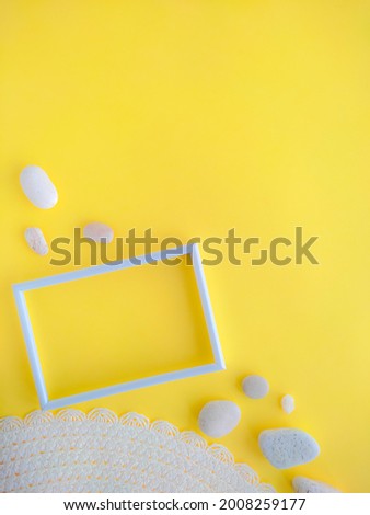 Empty white photo frame, hat, pebbles on a yellow background. Flatly. Summer concept