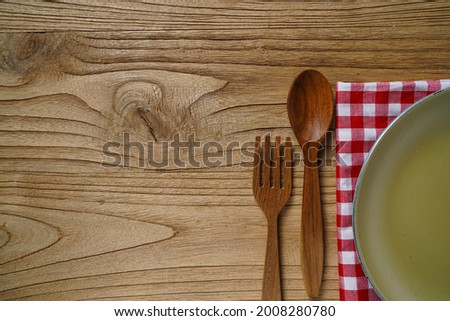 Light brown plates, red and white checkered napkins, wooden cutlery on a table or wooden pedestal. Indonesian tableware.