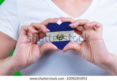 Woman in white t-shirt holds a heart in the form flag El Salvador on her chest. Photo for a postcard on Flag Day, Independence Day, travel, patriotism, other holiday