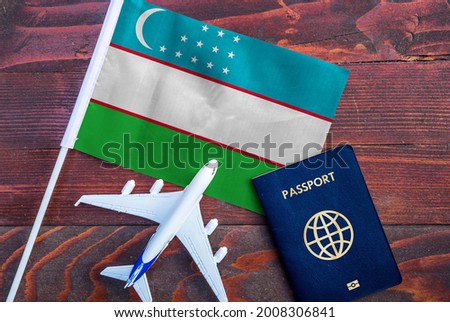 Flag of Uzbekistan with passport and toy airplane on wooden background. Flight travel concept 