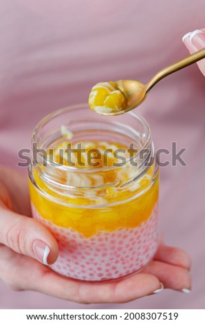 Jar of tapioca and pineapple jam. A woman is eating a healthy dessert from a jar with a teaspoon. Pleasant appetizing snack - tender mus