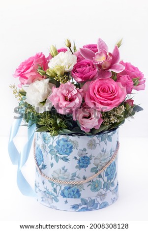 flowers in a blue box with ribbons on a white background, close-up with a blurred background. pink orchid, roses, eustoma, white eustoma, greens, as a gift for mother's day
