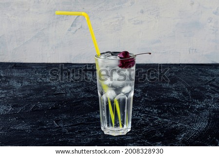 Clear glass with cherry, ice and yellow cocktail straw on black and white background. Summer cold drink and cocktail. copy space