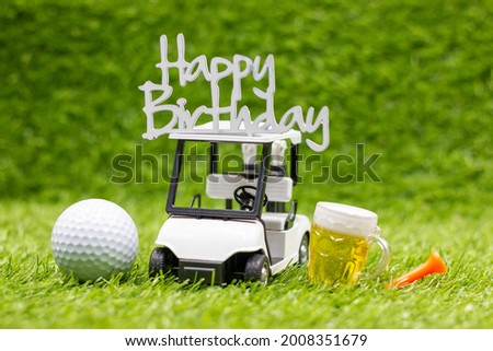 Happy Birthday sign on golf cart with golf ball and glass of beer on green grass 