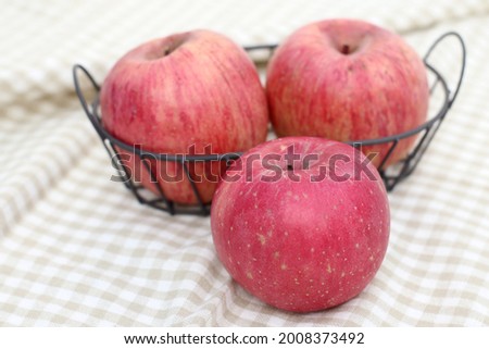 three Red apples in a wire basket on beige checker background. Close up view.