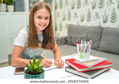  A beautiful little girl is studying at a cozy desk with books. School education at home or preparing for school on vacation