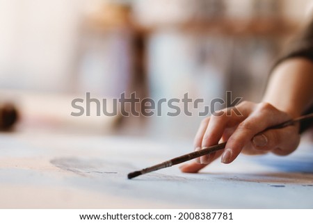 Woman hand artist painting while sitting on a floor at an art studio close up holding paintbrush