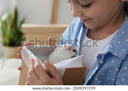 Happy little girl holding gift box with cute hamster at home