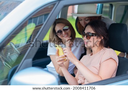 Three happy girlfriends go on a trip. Women are driving in a car and taking a selfie on a mobile phone