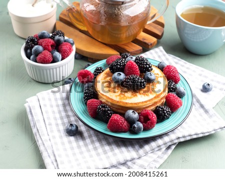 Stack of pancakes with raspberries and blueberries served with green tea.