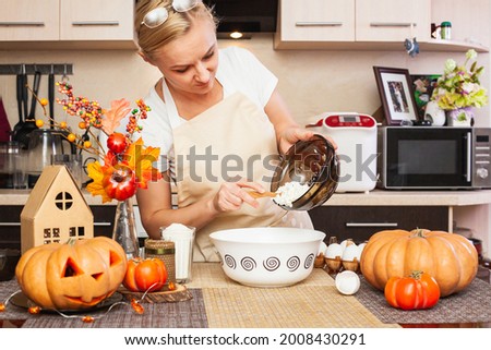 A woman puts cottage cheese in cookie dough for Halloween in the kitchen with autumn decor. Cozy home and preparation, Making cookies for Halloween.
