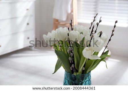 Beautiful bouquet of willow branches and tulips in vase indoors, space for text
