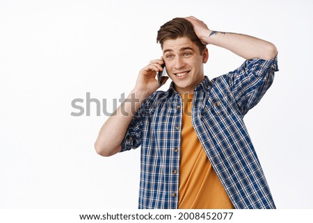 Awkward guy talking on mobile phone, calling someone and looking hesitant, touching head and look aside indecisive, dont know what to say, standing against white background