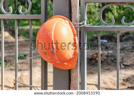A working construction helmet hangs on the fence. Completion concept. Builders protest about low wages. Builders Union - Compliance with Workers' Requirements Royalty-Free Stock Photo #2008453190