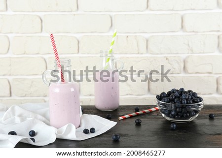 Two blueberry milkshake bottles on black wooden table. Couple of protein shake drinks with berries on kitchen counter. White brick wall background. Clean eating concept. Copy space, close up, top view