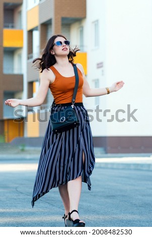 Full-length portrait fashionable girl. Carefree Caucasian lady plays with her hair during photo shoot. Beautiful girl expressing dancing. Urban background.