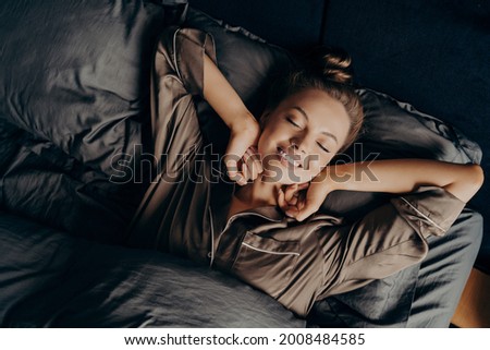 Good morning. View from above of young beautiful relaxed brunette female with closed eyes in satin pajamas waking up in her bed fully rested, happy woman stretching after night sleep Royalty-Free Stock Photo #2008484585