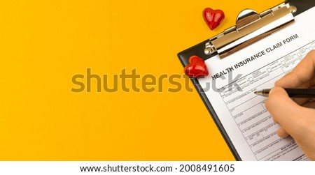 Health insurance form. Business desktop with clipboard, pen and red hearts on a yellow desktop. Top view and copy space 