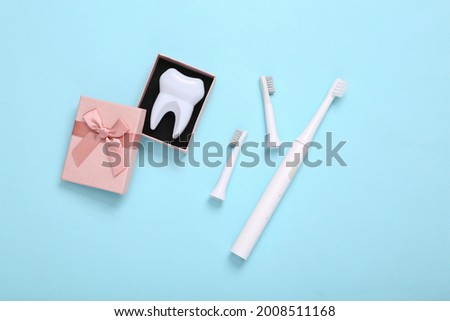 Ultrasonic plastic toothbrush with replaceable heads and tooth model in gift box on blue background. Dental care concept. Top view