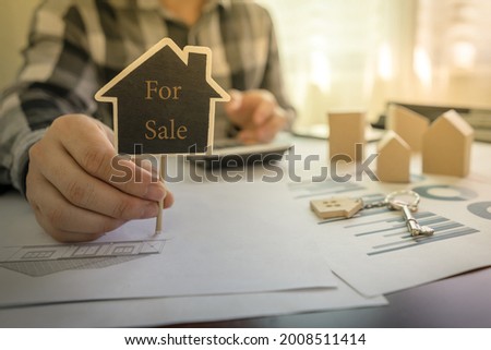 Real estate agents showing message For Sale on the sign of house shape on the table with a calculator, key, house design document, home wooden model.