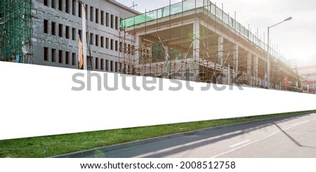 Long blank hoarding with space for advert mockup on construction site under unfinished building with scaffold