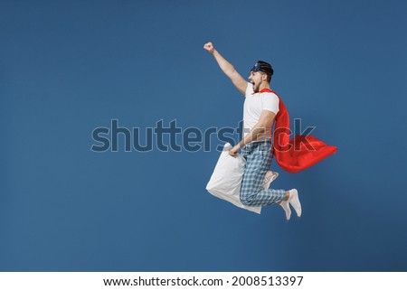 Full length powerful young man in pajamas jam sleep mask superhero suit rest home jump high fly on pillow have supernatural abilities isolated on dark blue background Good mood night bedtime concept.