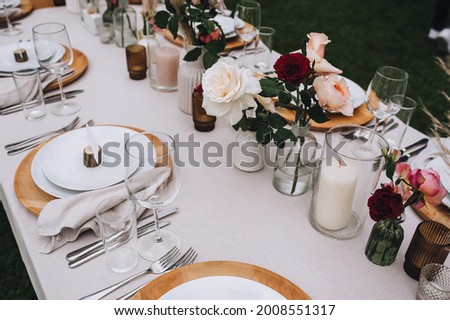 A set of dishes, cutlery and accessories on a wooden table with a tablecloth - empty plates, forks, knives, glasses, roses in vases, candles in candlesticks. Photography, concept.