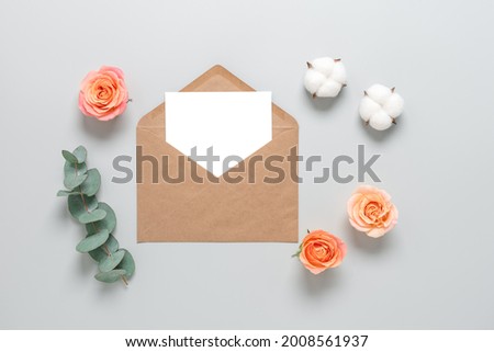 Blank card mockup in an envelope on a gray background decorated with roses, cotton flowers and eucalyptus branch. Wedding stationery template. Top view, flat lay