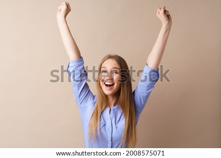 Surprised young blonde woman throwing up her hands against beige background
