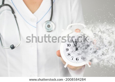 Time is crucial life saver. Concept healthcare. Doctor in white coat with stethoscope pointing and dissolving alarm clock. Time is running out concept.