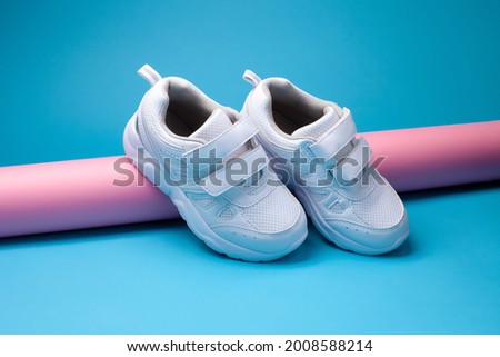 the composition is a balance of two white children's sneakers with Velcro fasteners for easy footwear on a pink, long paper roll on a blue background.