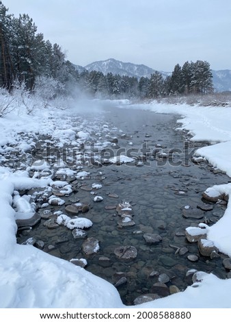 An unfrozen mountain river, with frost-covered trees and bushes along the banks, on a frosty winter morning. Travel concept.