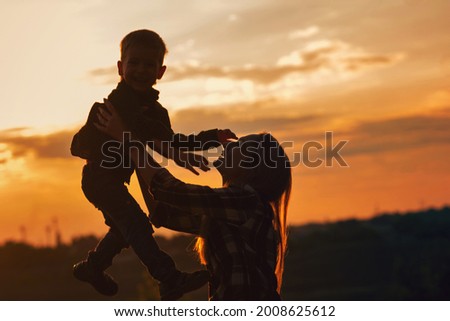 Silhouette young mother with pleasure spending time with kid in park. Lovely Mommy throw up son against sunset. Happy childhood moments, having fun together. Enjoying life