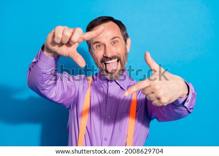 Photo of excited mature man happy positive smile fooling tongue-out gesture fingers frame picture isolated over blue color background