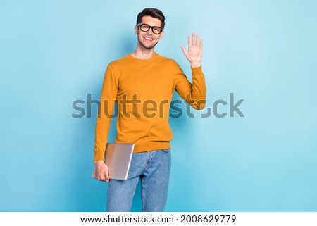 Photo of young cheerful man happy positive smile hold laptop waving hand hello isolated over blue color background Royalty-Free Stock Photo #2008629779