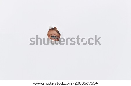 The right eye. Voyeurism. The man is watching the wife. A curious look. Jealousy, spying on or overhearing the concept. Hole on white paper. Royalty-Free Stock Photo #2008669634