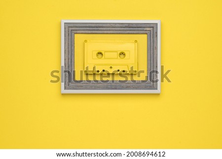 A yellow tape cassette in a frame on a yellow background. Stylish retro equipment for listening to music. Flat lay.
