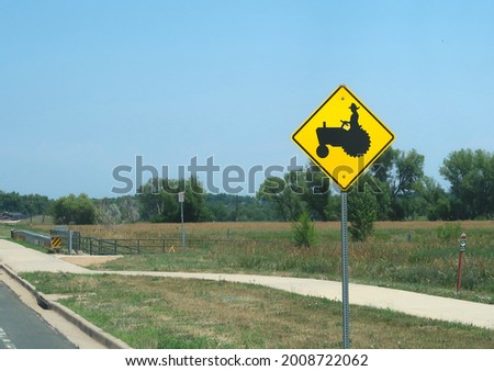 Caution street sign for tractor crossing near farm land                               