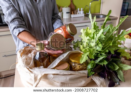 Adult woman pulls out the purchased products from farmers market from the fabric bags. Eco-friendly shopping. Zero waste concept. Conscious consumption. Royalty-Free Stock Photo #2008727702