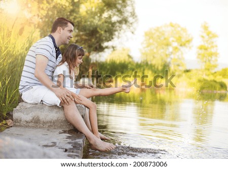 Happy young father sitting by the lake with his little daughter