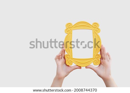 a hand holds a yellow frame from the TV series friends