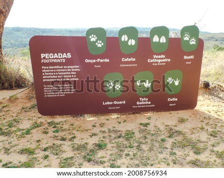 Sign: Board demosntrativa, indicative of the marks and footprints of animals that inhabit the old villa State Park Brazil, marron green card, with writing in white and subtitles Portuguese and English