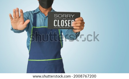 Asian man holding notice board sorry we are closed sign hanging a restaurant, store, office or other, business open back to new normal after coronavirus, covid-19. with clipping path
