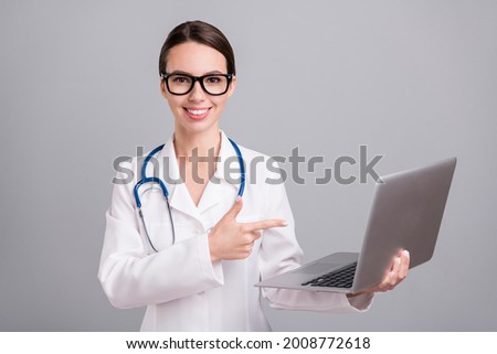 Photo portrait young nurse with sthethoscope smiling showing finger laptop isolated grey color background