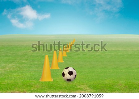 Old football on the green grass with funnel or cone for practice skill in meadow with blue sky and clouds background 